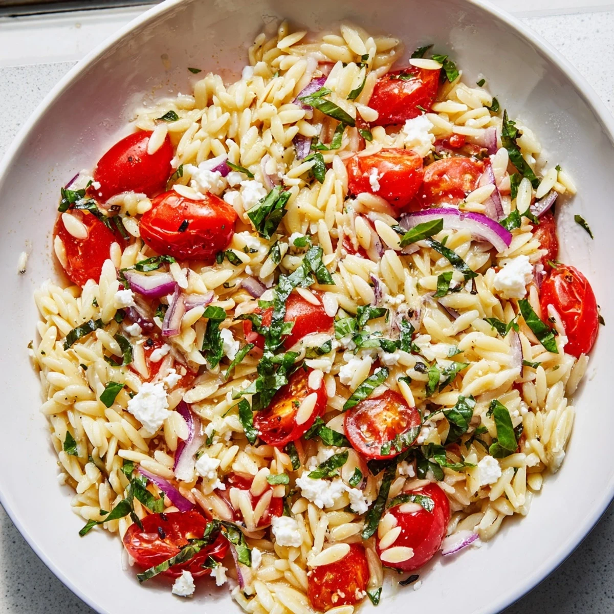 Bright and colorful Tomato Feta Orzo salad with crumbled feta and fresh basil for serving.