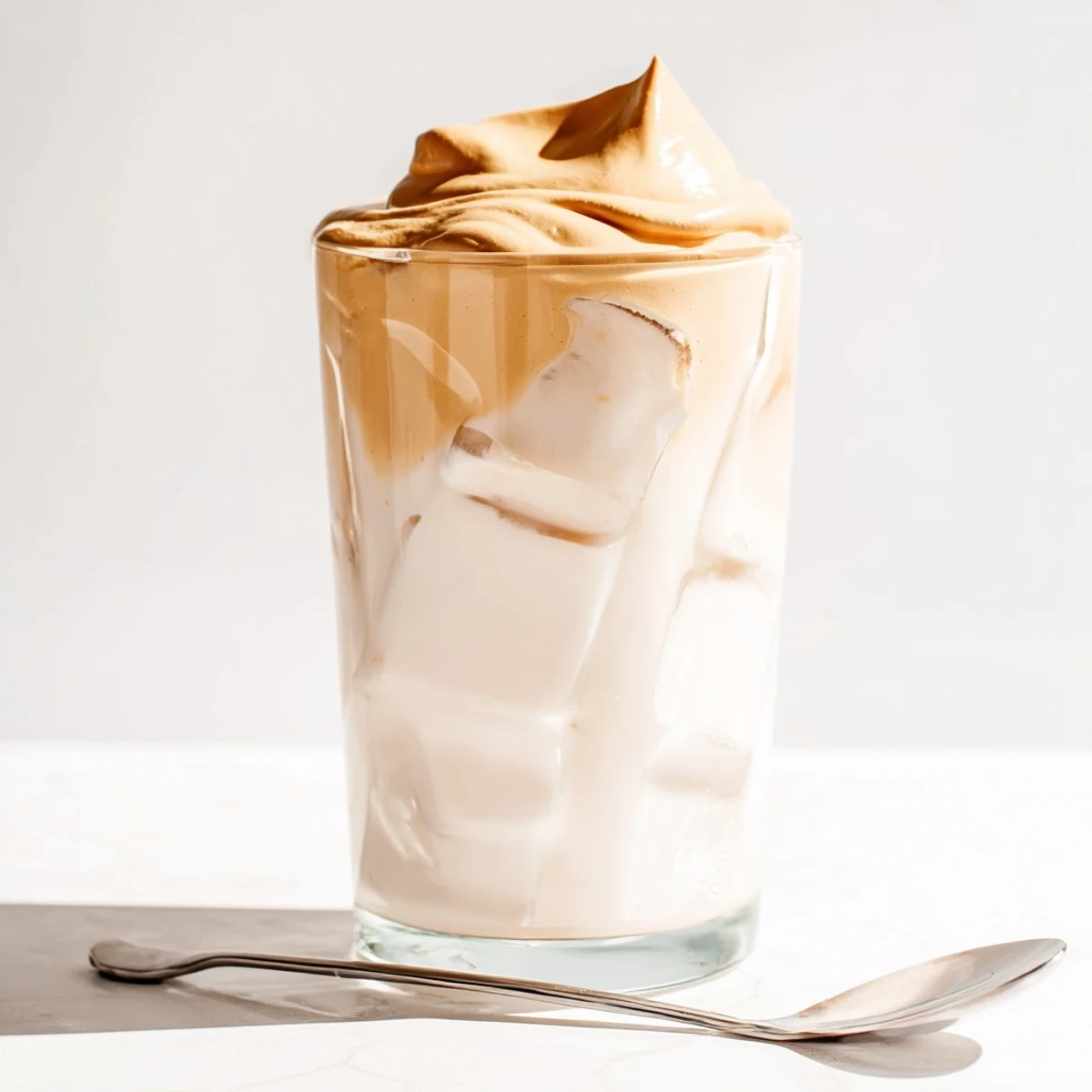 Café-style Dalgona coffee served over ice, with a soft, whipped coffee topping melting into the milk below.