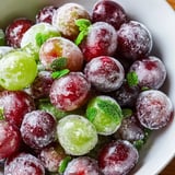 Freshly frozen Frozen Grapes Spa Treat on a baking sheet with mint garnish, ready to be enjoyed as a cool, spa day treat.