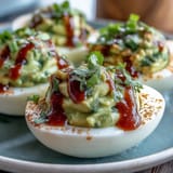 Creamy avocado deviled eggs topped with spicy Sriracha drizzle for a vibrant appetizer.  