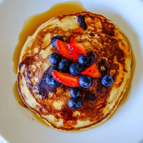 Golden brown banana pancakes stack neatly on a white plate, topped with fresh blueberries and a drizzle of maple syrup.  