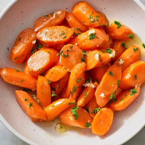 Golden Honey-Glazed Carrots glistening in a pan, coated with a sweet honey glaze and herbs.