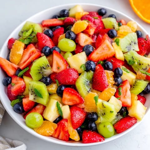 A chilled bowl of refreshing fruit salad, showcasing a glistening honey-lime glaze over juicy sliced fruits.