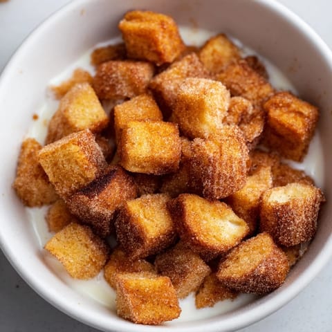A breakfast bowl full of mini French toast cereal cubes, warm and inviting with a dusting of cinnamon.