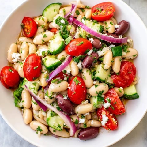 This vibrant white bean salad shows a close-up of colorful ingredients mixed with dressing.