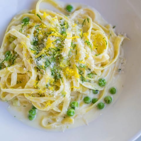 A mouthwatering close-up of creamy dill pasta with bright green dill and peas.