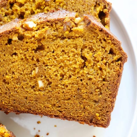 Slice of tender pumpkin bread loaf, perfect for an autumn snack, paired with a steaming cup of coffee.