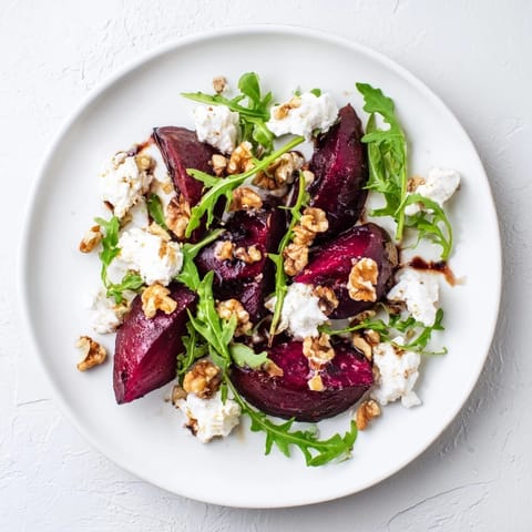 A close-up of a vibrant roasted beet goat cheese salad with glistening balsamic glaze on ruby-red beet cubes and crumbled tangy cheese.
