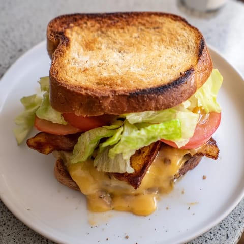 A close-up view shows the Vegan Bacon BLT Grilled Cheese, featuring smoky tempeh strips and fresh tomato slices between cheesy, buttery bread, ideal for a hearty lunch.