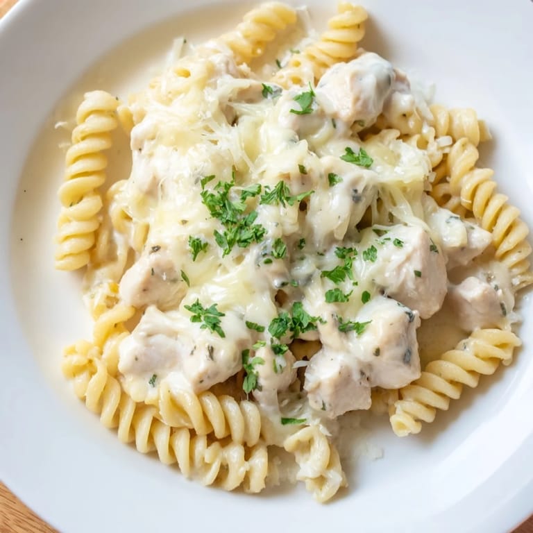 A close-up of a flavorful Chicken Alfredo Bake showing cheesy, bubbly topping and tender pasta and chicken.