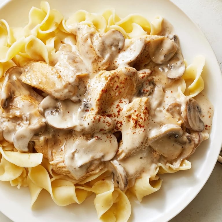 A close-up of Chicken and Mushroom Stroganoff reveals tender poultry pieces and earthy fungi coated in a velvety, sour cream-based gravy.