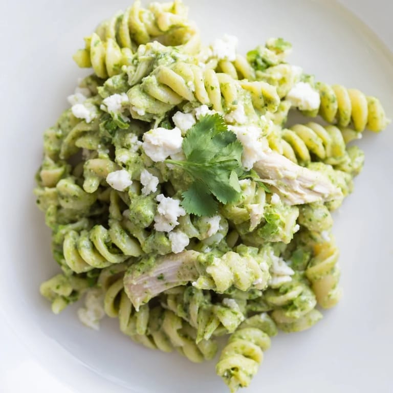 A close-up of cilantro lime chicken pasta featuring rotini coated in tangy Greek yogurt sauce, topped with crumbled cotija and extra chopped cilantro.